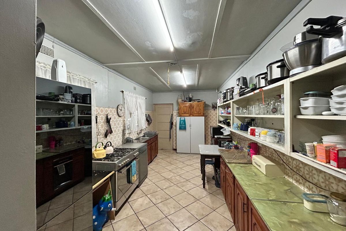 A dated galley-style kitchen featuring traditional wooden cabinetry, tiled flooring, and extensive open shelving, offering a functional layout with significant potential for modernization.