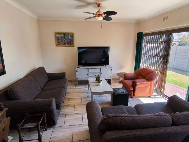 A comfortable living room featuring tiled flooring, a ceiling fan, and large sliding glass doors providing access to the rear garden.