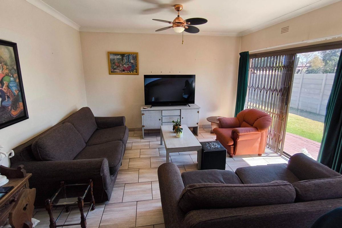 A comfortable living room featuring tiled flooring, a ceiling fan, and large sliding glass doors providing access to the rear garden.
