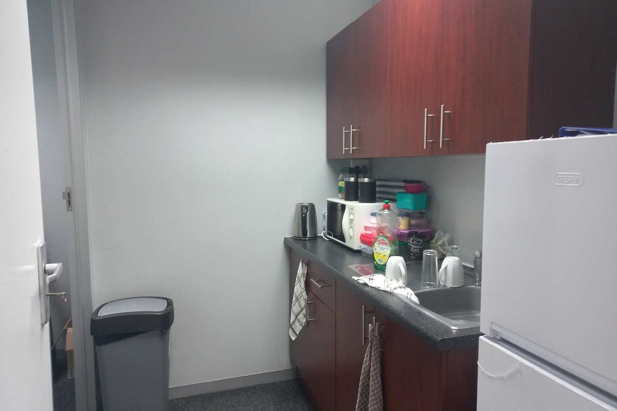 A compact office kitchenette featuring dark wood cabinetry, a laminate countertop, and a stainless steel sink.