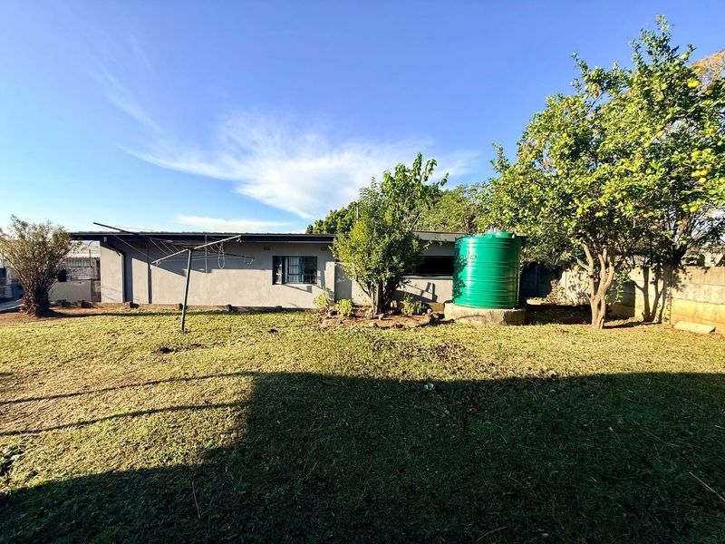 Rear garden view featuring a lawn area, mature trees, a water storage tank, and a rotary clothesline against the rear building facade.
