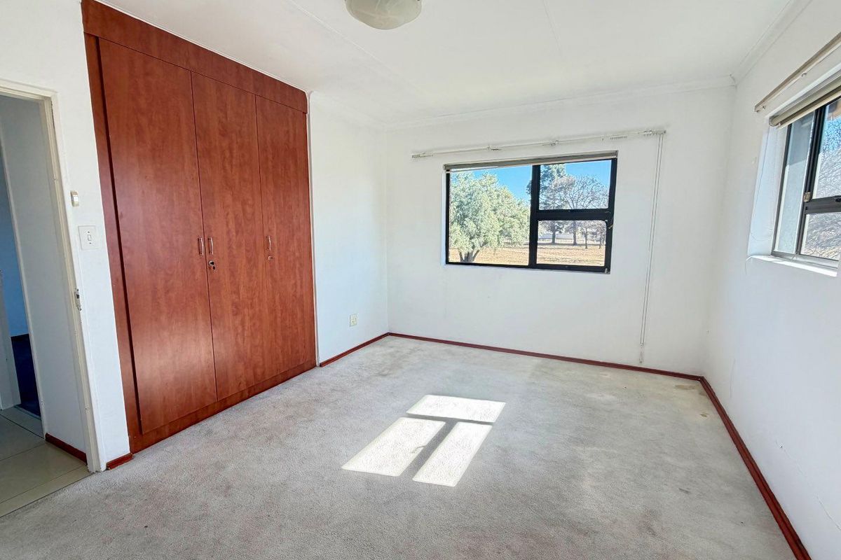 A vacant bedroom featuring built-in wooden cupboards, carpeted flooring, and natural light from the window.