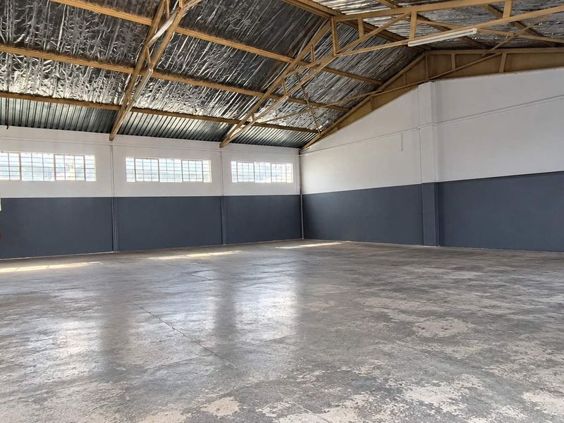 Spacious industrial warehouse unit featuring high exposed steel roof trusses, durable concrete flooring, and ample natural light through industrial-style windows.