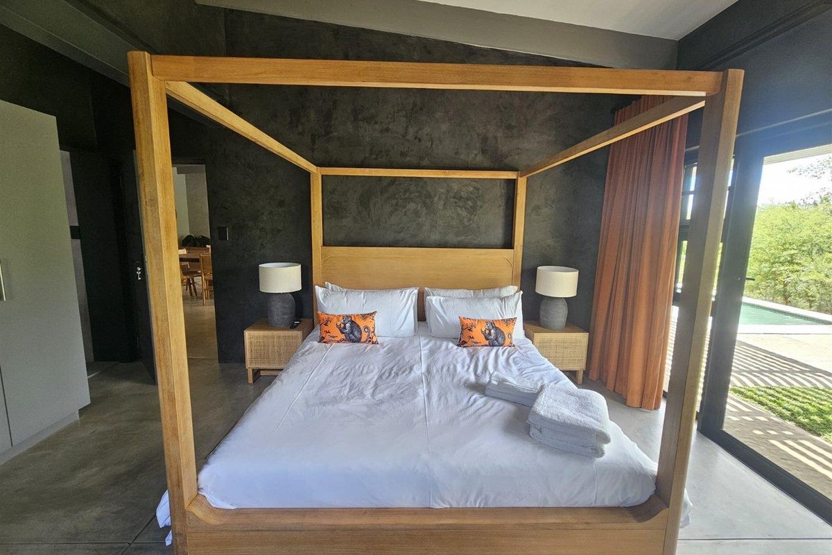 Spacious bedroom featuring polished concrete floors, a dark textured feature wall, and large sliding glass doors providing direct access to the outdoor pool area.