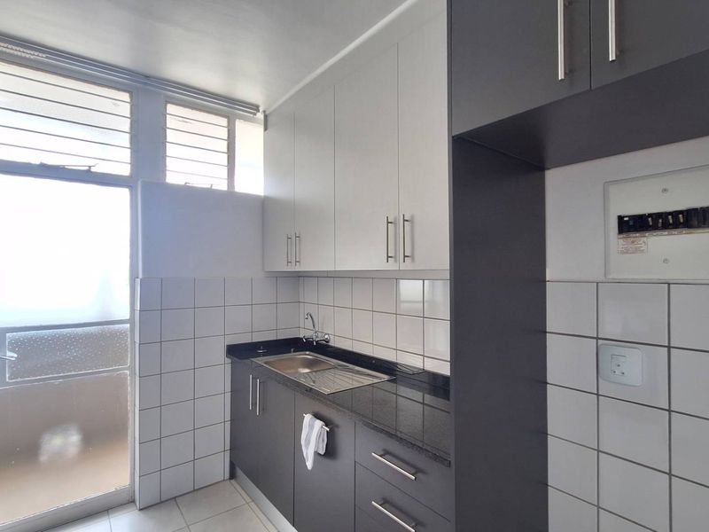 A clean and functional scullery area featuring modern dark and light cabinetry, granite countertops, a stainless steel sink, and tiled wall finishes.