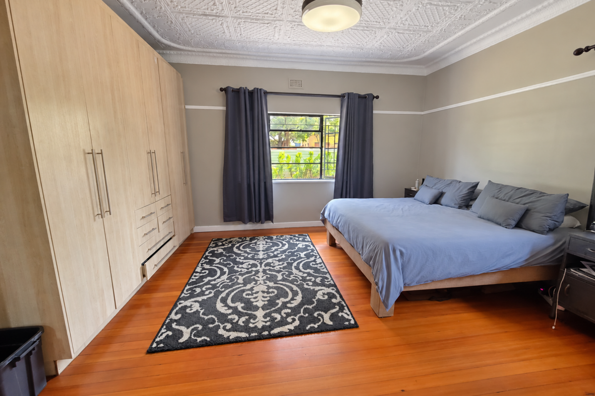 Spacious bedroom featuring polished timber flooring, classic pressed metal ceilings, and extensive built-in wardrobe storage.