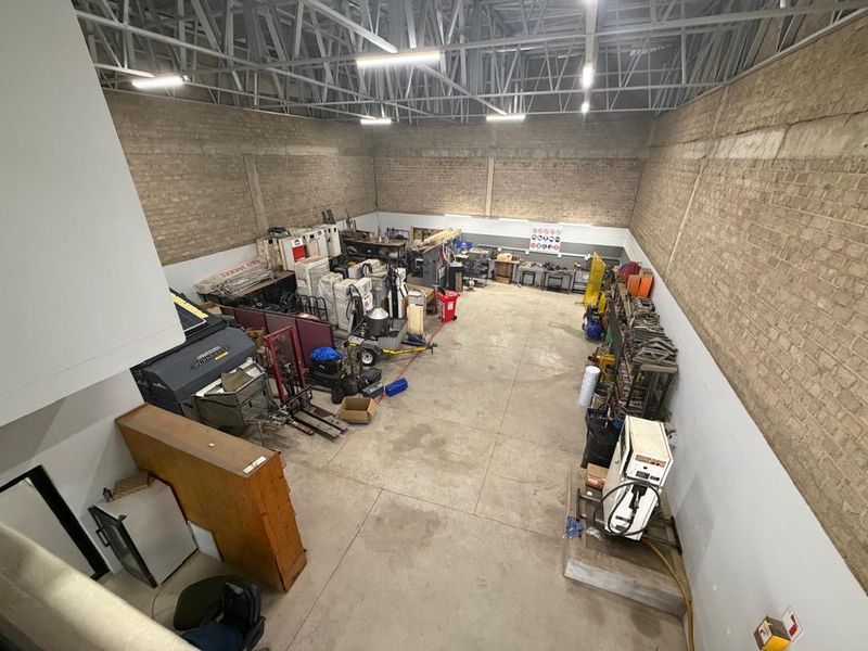 Spacious industrial utility area featuring exposed brick walls, high ceilings with steel trusses, and durable concrete flooring, suitable for workshop or storage use.