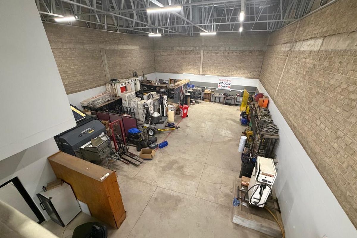 Spacious industrial utility area featuring exposed brick walls, high ceilings with steel trusses, and durable concrete flooring, suitable for workshop or storage use.