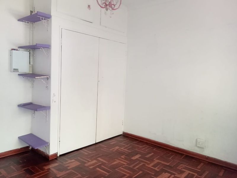 A vacant bedroom featuring classic parquet flooring, built-in storage cupboards, and wall-mounted shelving units.