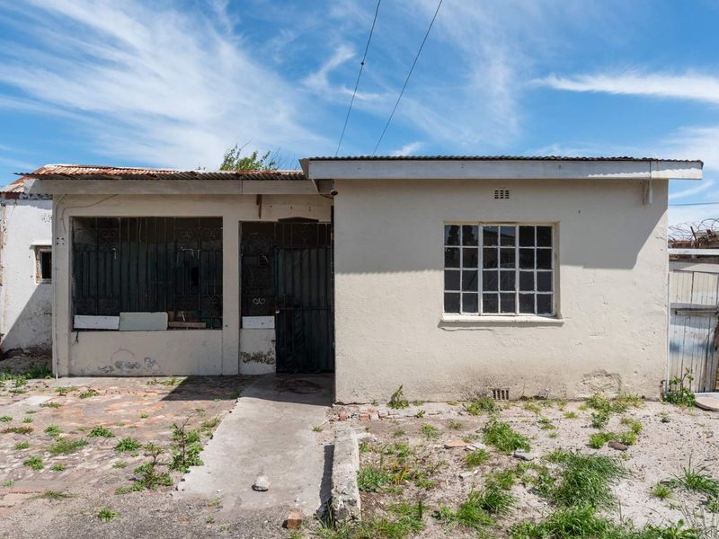 Front elevation of a single-story house featuring a corrugated metal roof, security bars on windows, and a weathered exterior finish requiring maintenance.