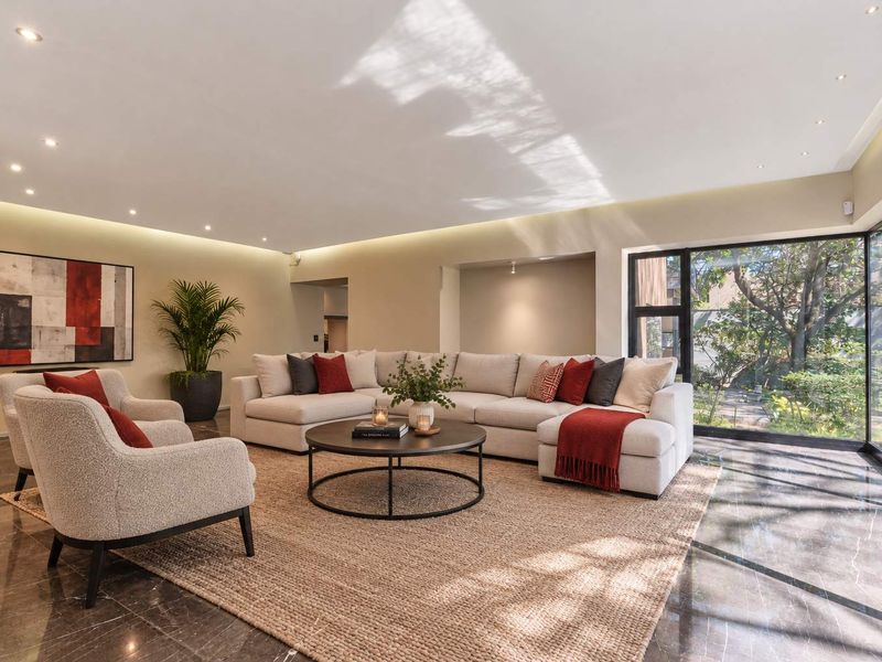 Spacious living room featuring polished marble flooring, recessed and cove lighting, and large floor-to-ceiling windows with views of the garden.