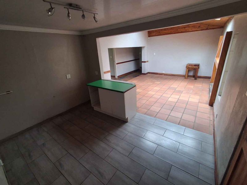 An open-plan living area featuring a mix of ceramic and terracotta flooring, a built-in breakfast counter, and exposed timber ceiling beams.