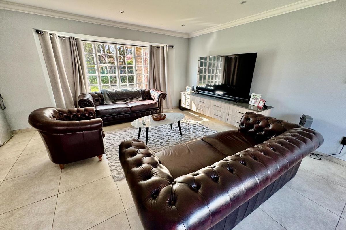 A spacious living room featuring large windows, tiled flooring, and recessed ceiling lighting, providing a bright and comfortable area for relaxation.