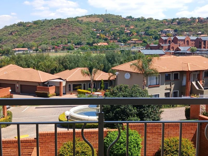 Elevated view from a balcony overlooking a residential townhouse complex with landscaped grounds and surrounding hills.