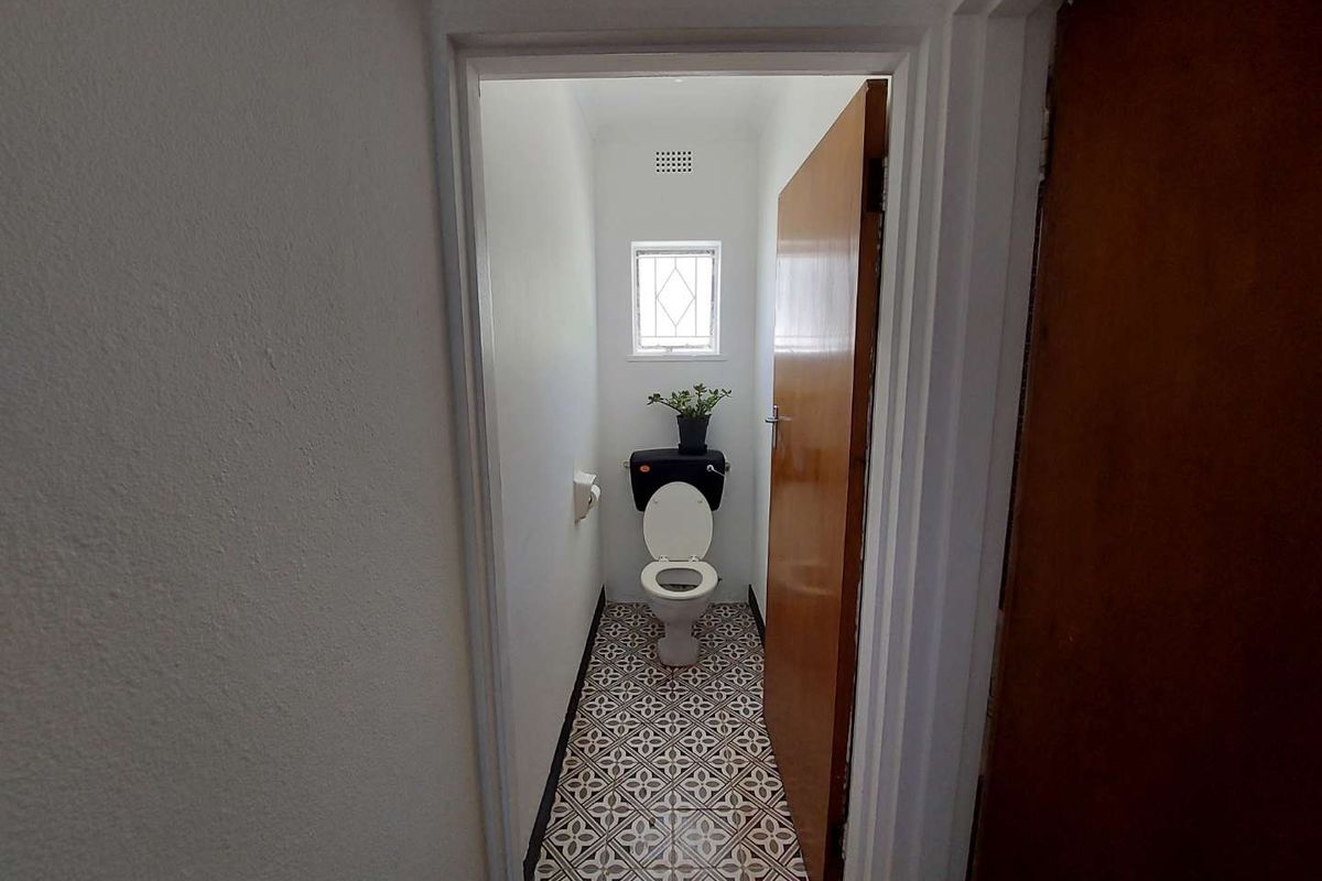A compact bathroom featuring patterned floor tiles, a standard toilet, and a small window for natural light.