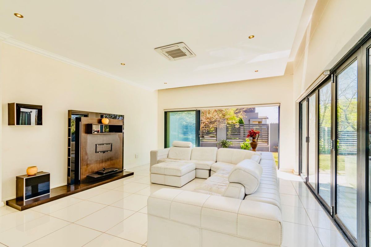 Spacious living room featuring large format floor tiles, recessed ceiling lighting, a built-in media unit, and expansive sliding glass doors opening to the garden.