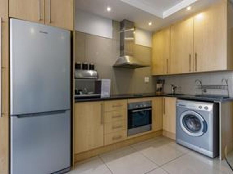 A compact, functional kitchen featuring light wood cabinetry, stainless steel appliances, tiled flooring, and recessed lighting.