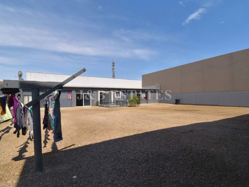 A large, open outdoor area featuring a gravel surface, perimeter boundary walls, and a rear building elevation with sliding glass doors.