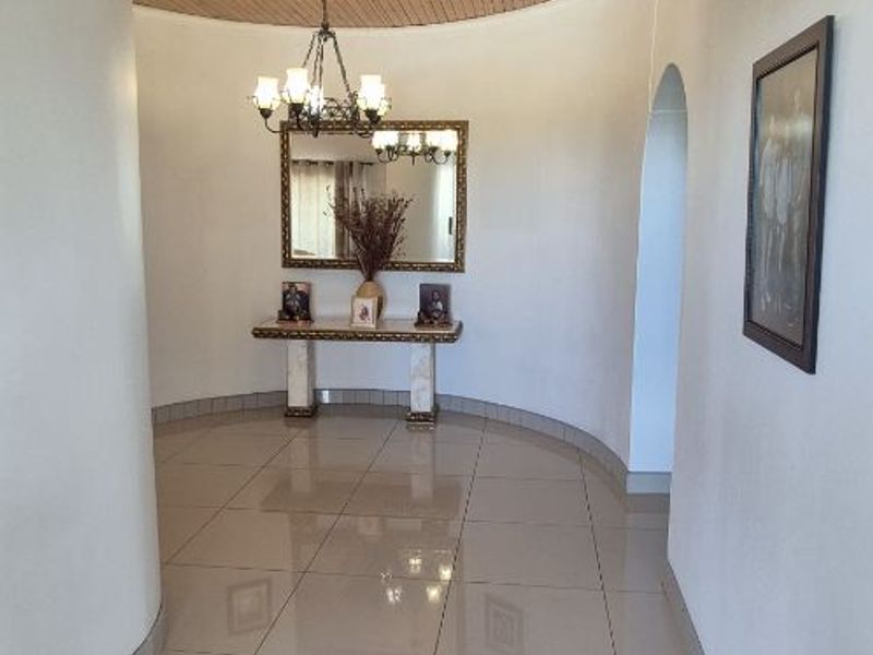 A spacious hallway featuring a distinctive curved wall, polished tile flooring, and a warm timber tongue and groove ceiling with an arched entryway.