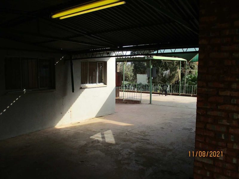 A covered outdoor patio area featuring a corrugated metal roof, concrete flooring, and metal security railings, offering a functional space for outdoor living.