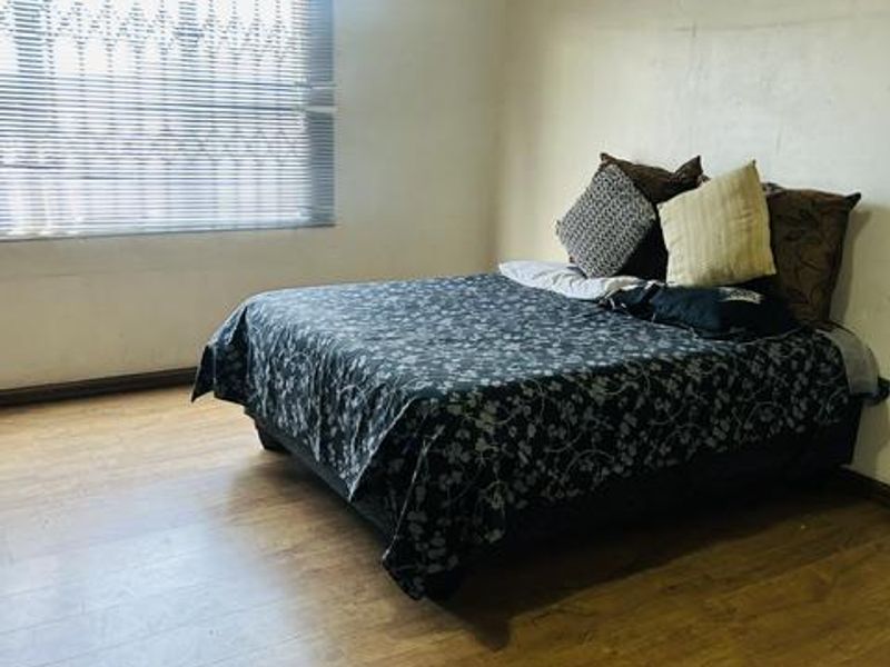 A bedroom featuring laminate flooring, a patterned ceiling, and a window fitted with venetian blinds and a security gate.