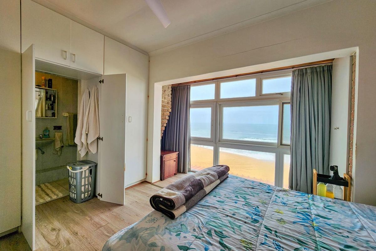 Bedroom featuring built-in cupboards, an en-suite bathroom, and large windows offering direct ocean views.