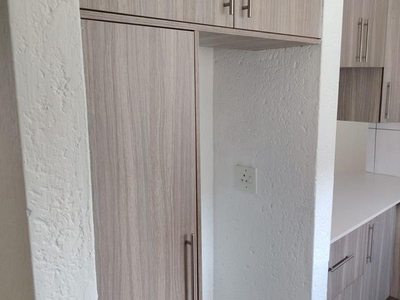 A clean kitchen area featuring modern wood-look built-in cabinetry, ample counter space, and tiled flooring in a well-maintained townhouse setting.