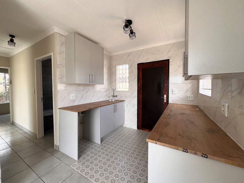 A clean, functional kitchen featuring light grey cabinetry, wood-look laminate countertops, marble-effect tiled backsplash, and patterned floor tiles.