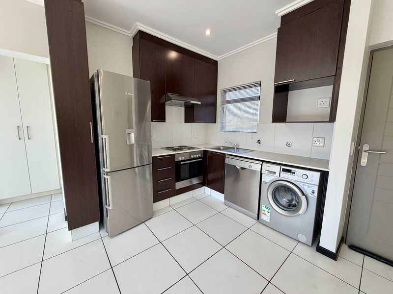 Modern kitchen featuring dark wood cabinetry, stainless steel appliances, tiled flooring, and a functional layout with integrated storage and workspace.