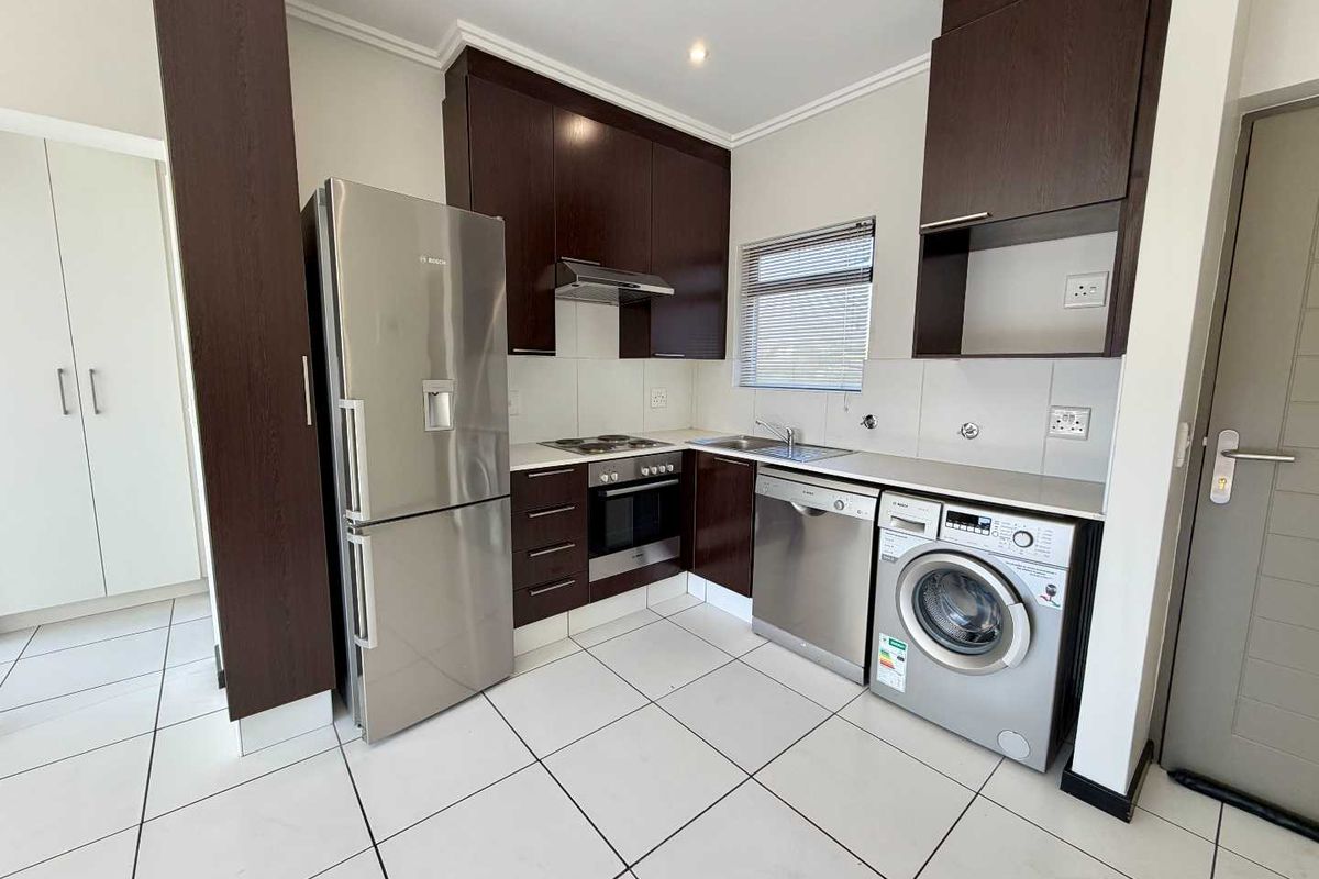 Modern kitchen featuring dark wood cabinetry, stainless steel appliances, tiled flooring, and a functional layout with integrated storage and workspace.