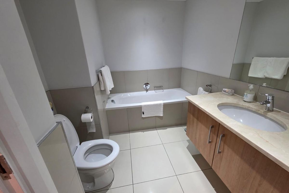 A clean, functional bathroom featuring a built-in bathtub, a vanity with a stone countertop, and neutral ceramic tiling throughout.