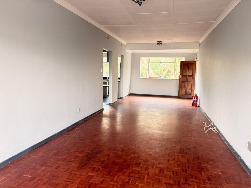 An empty living room featuring traditional parquet flooring, neutral wall tones, and a timber entrance door, offering a blank canvas for interior design.