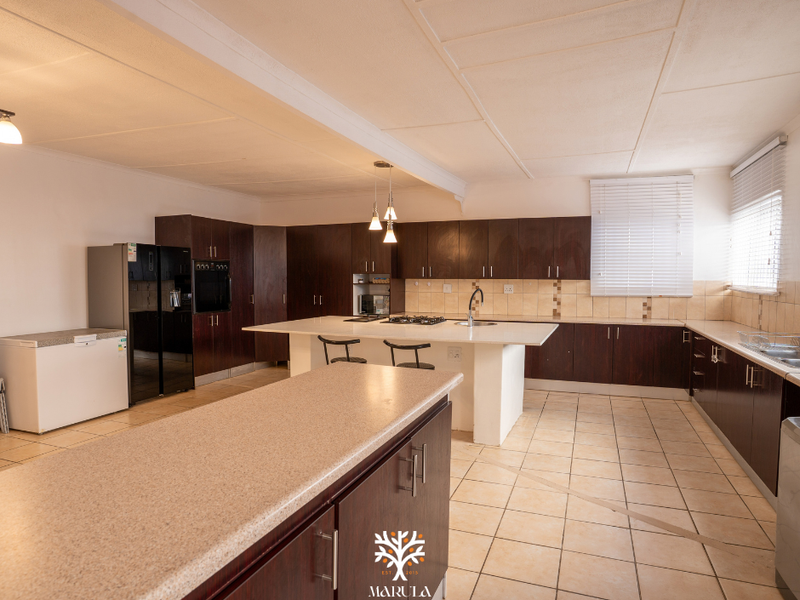 Spacious kitchen featuring dark wood cabinetry, a large central island with stone countertops, gas cooktop, and tiled flooring throughout.