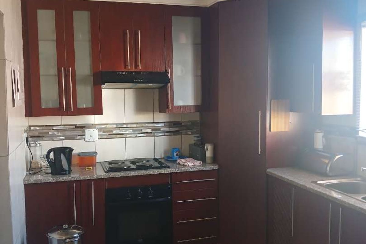 A functional kitchen featuring dark wood cabinetry, granite countertops, a built-in oven, hob, and extractor fan with tiled backsplash.