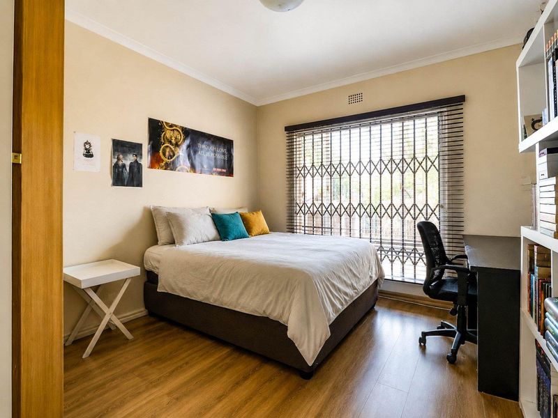 A functional bedroom featuring laminate flooring, built-in shelving, and a window fitted with security gates and venetian blinds.