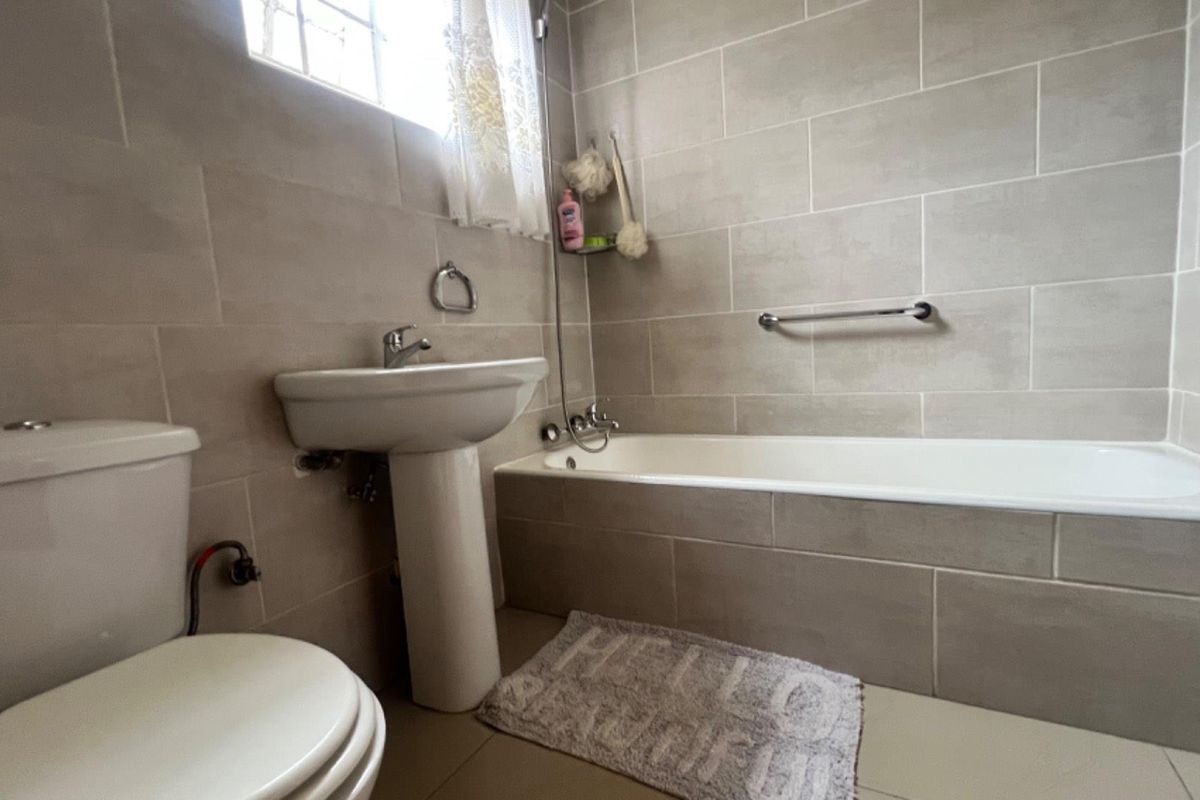 A functional bathroom featuring neutral wall tiles, a pedestal washbasin, a standard toilet, and a built-in bathtub with a wall-mounted grab bar.