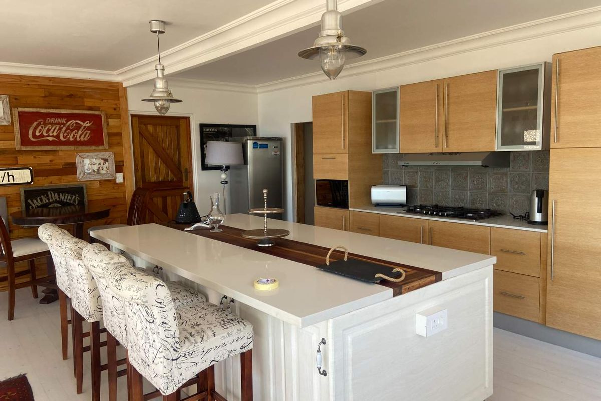 Modern kitchen featuring a large central island with stone countertop, light wood cabinetry, integrated gas hob, and decorative tiled backsplash.