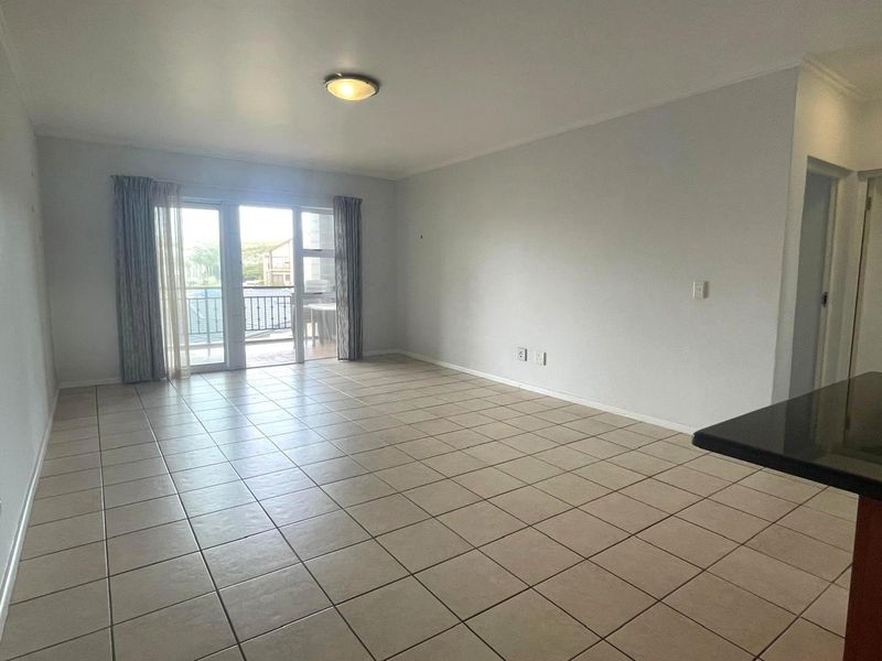Spacious open-plan living area featuring neutral ceramic floor tiles, a flush mount ceiling light, and direct access to a private balcony through sliding glass doors.