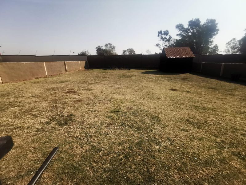 A spacious, level backyard featuring a perimeter wall with electric fencing and a small garden shed, offering significant potential for landscaping.