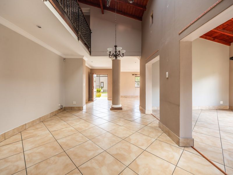 Spacious open-plan living area featuring double volume ceilings with exposed timber beams, tiled flooring, and a mezzanine level with wrought iron railing.