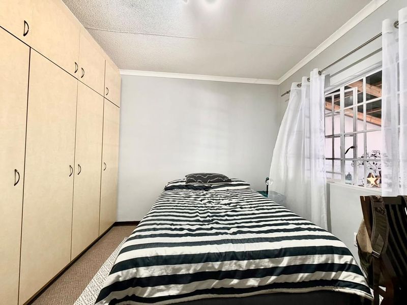 A functional bedroom featuring floor-to-ceiling built-in cupboards and a window fitted with security bars.
