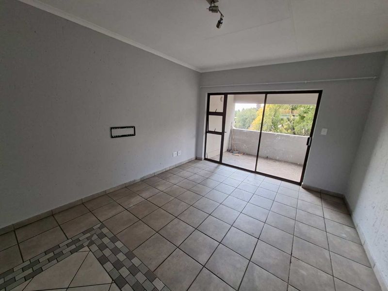 An empty, tiled living room featuring a sliding glass door that opens onto a balcony, providing natural light and access to outdoor space.