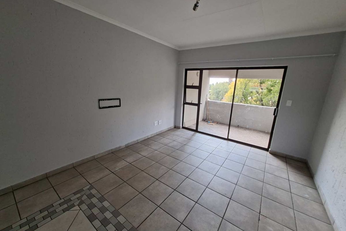 An empty, tiled living room featuring a sliding glass door that opens onto a balcony, providing natural light and access to outdoor space.
