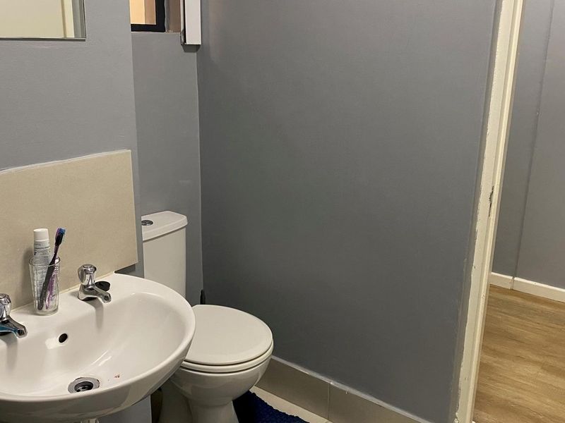 A functional bathroom featuring a pedestal washbasin with a tiled splashback, a standard toilet, and neutral grey wall finishes.