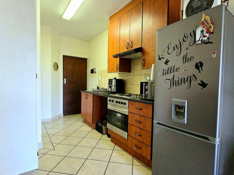 A functional kitchen featuring wooden cabinetry, a built-in oven with hob, extractor fan, and tiled flooring.