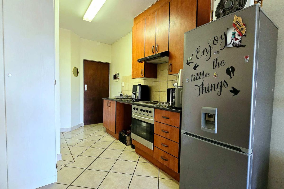 A functional kitchen featuring wooden cabinetry, a built-in oven with hob, extractor fan, and tiled flooring.
