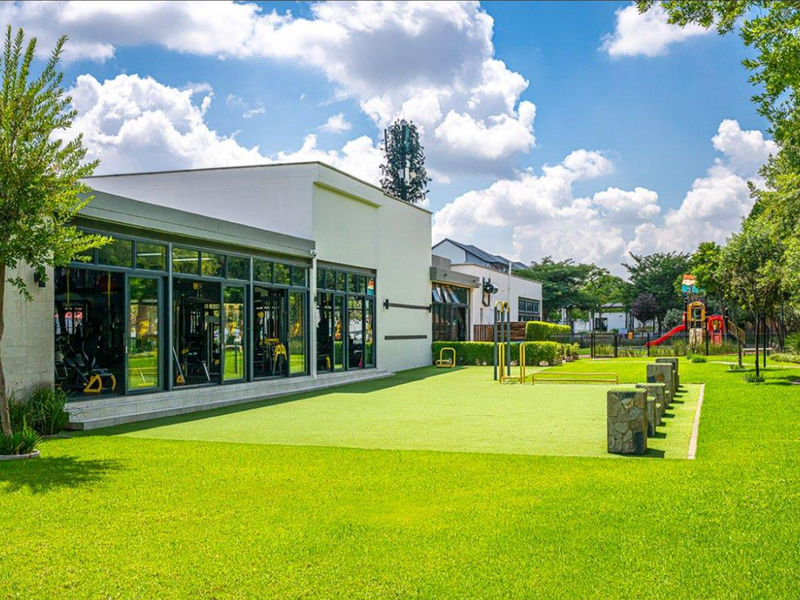 A well-maintained communal garden area featuring artificial turf, stone bollards, and large glass doors providing access to the gym facility.