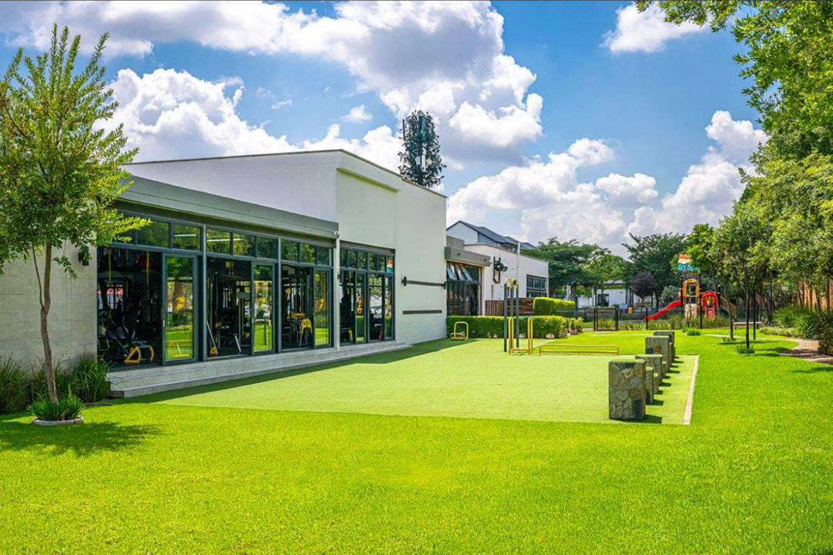 A well-maintained communal garden area featuring artificial turf, stone bollards, and large glass doors providing access to the gym facility.