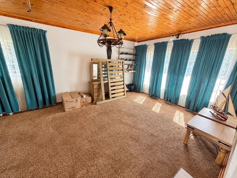 Spacious living room featuring a warm timber tongue and groove ceiling, carpeted flooring, and a decorative wrought iron chandelier.