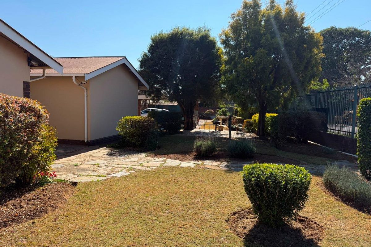 A rear garden area featuring a stone paved pathway, established trees, and metal perimeter fencing, providing a private outdoor space.